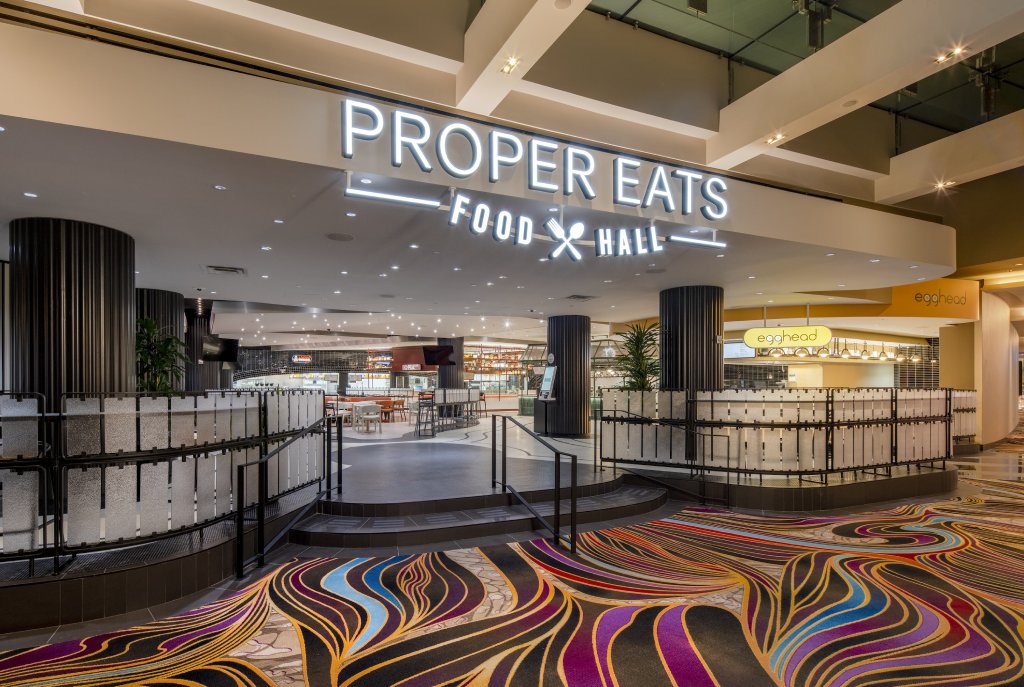 The entry of the Proper Eats Food Hall in the Las Vegas aria shows colorful carpet below and modern signage above modern architecture.