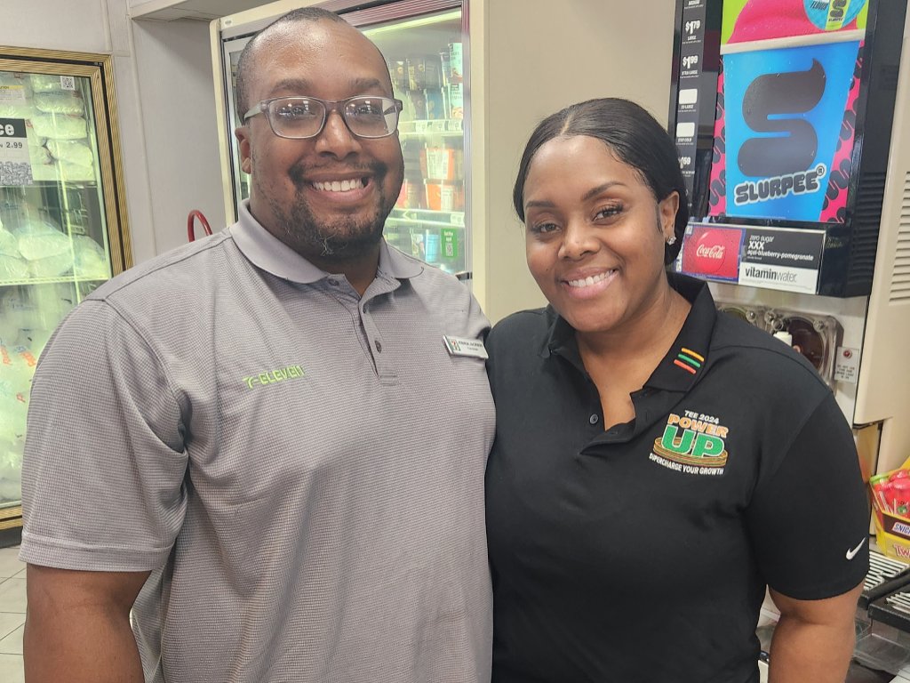 A lovely black couple stands in their North Las Vegas 7-11 store. They are wearing polo shirts and smiling.